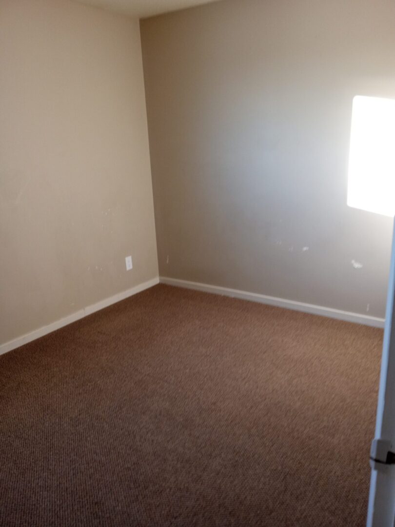 An empty room with tan carpet and a window.